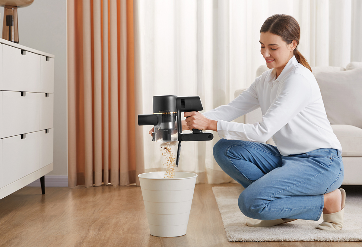 Απεικονίζεται μια γυναίκα να αδειάζει το δοχείο της σκούπας σε έναν κάδο.